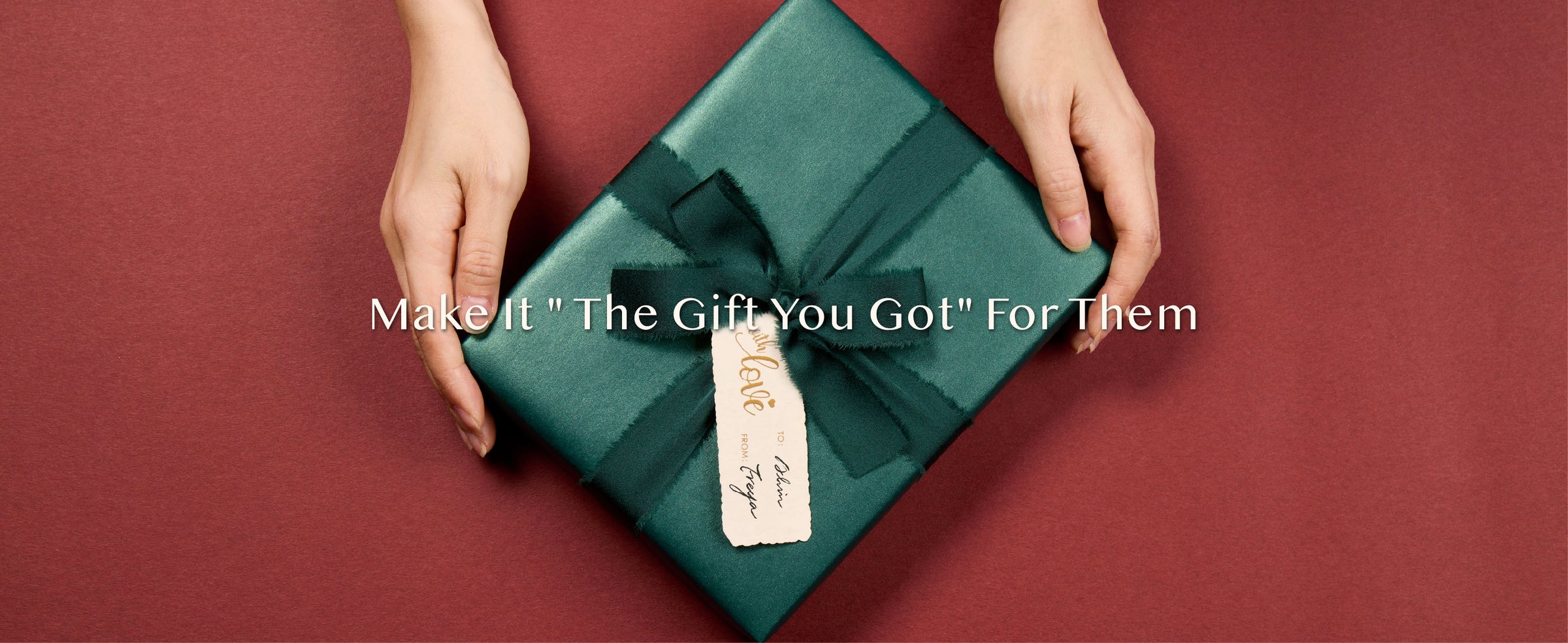 Hands presenting a gift in shimmering green paper with a dark green bow and cream tag