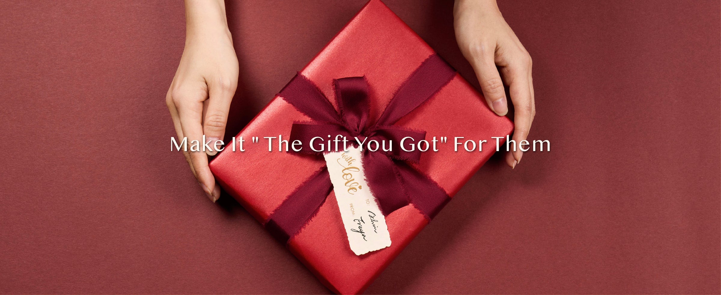 Hands presenting a gift in shimmering red paper with a burgundy bow and cream tag