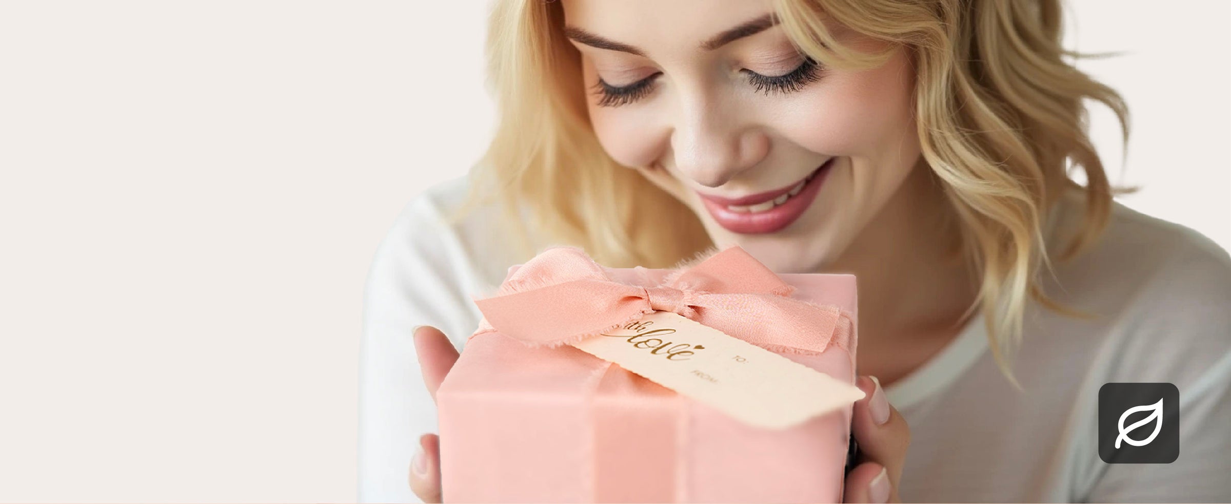 Smiling woman holding a gift wrapped in pearly pink paper with a pink bow and cream tag