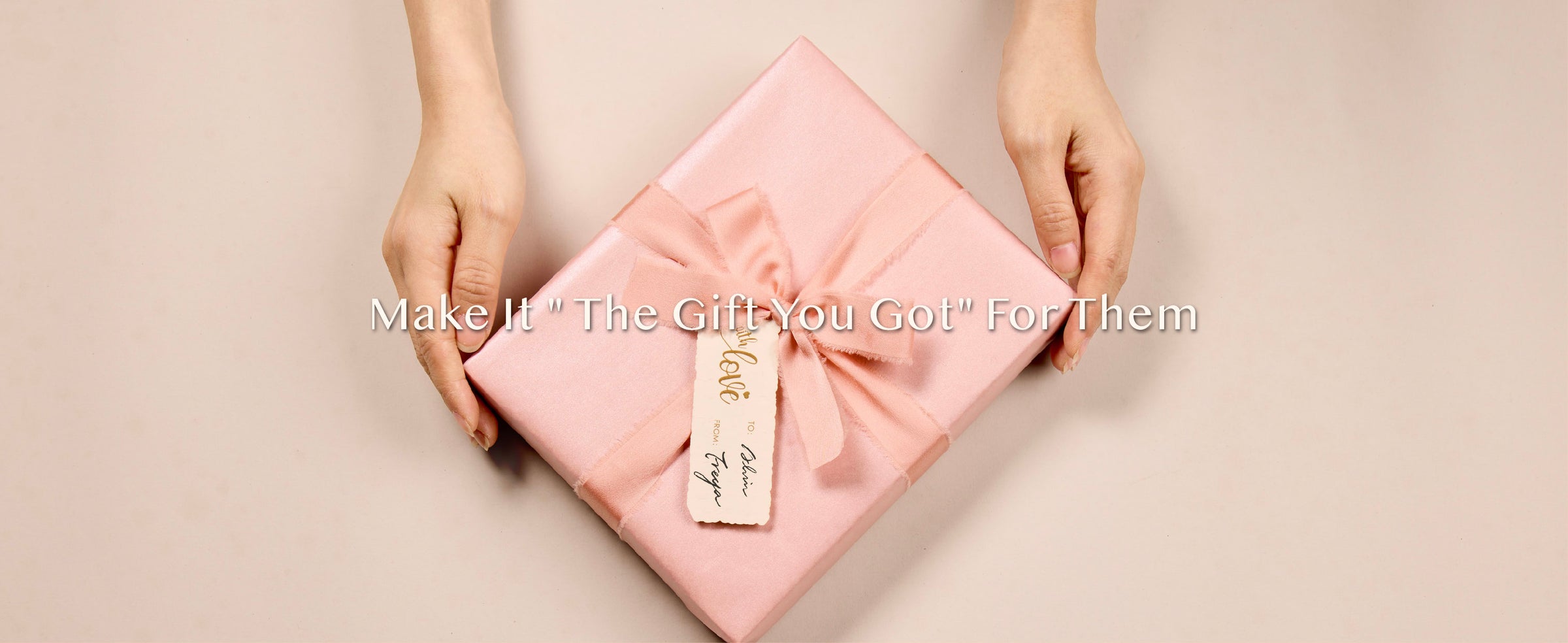 Hands presenting a square gift wrapped in pearly pink paper with a matching bow and tag