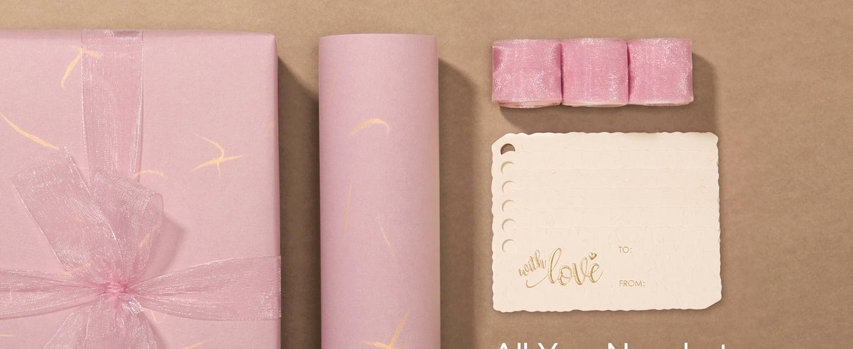Pink gold-accented wrapping paper set with sheer ribbon, scalloped tags, and a wrapped gift.