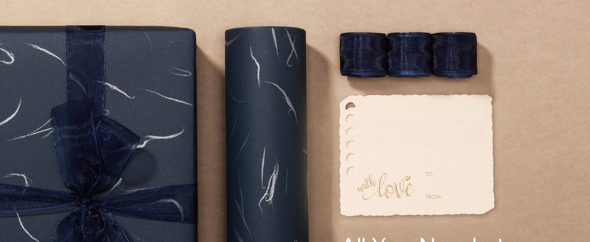 Navy wrapping paper set with silver accents, organza ribbon, gift tags, and a wrapped present.