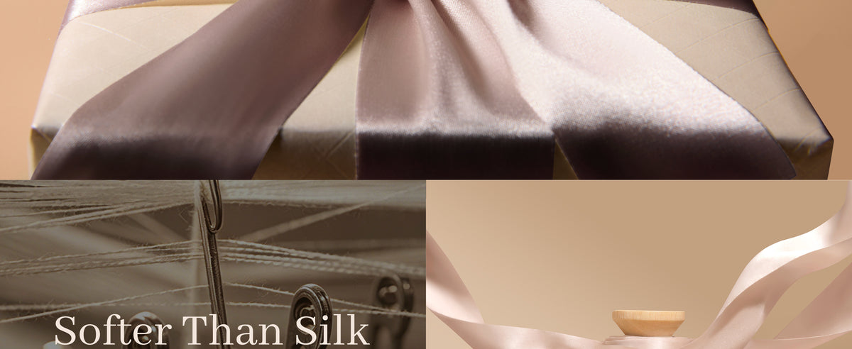 Close-up of champagne-nude satin ribbon draped over a box, with textile machinery behind it.