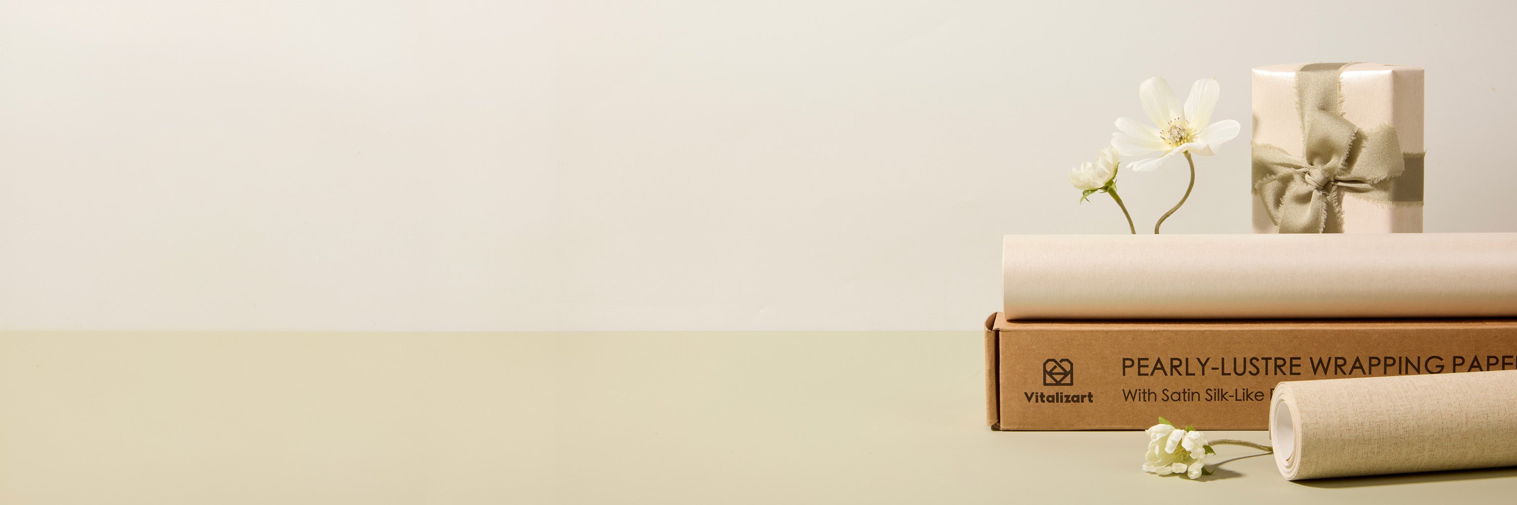 Pearlescent wrapping paper rolls and a ribbon-wrapped gift beside white flowers