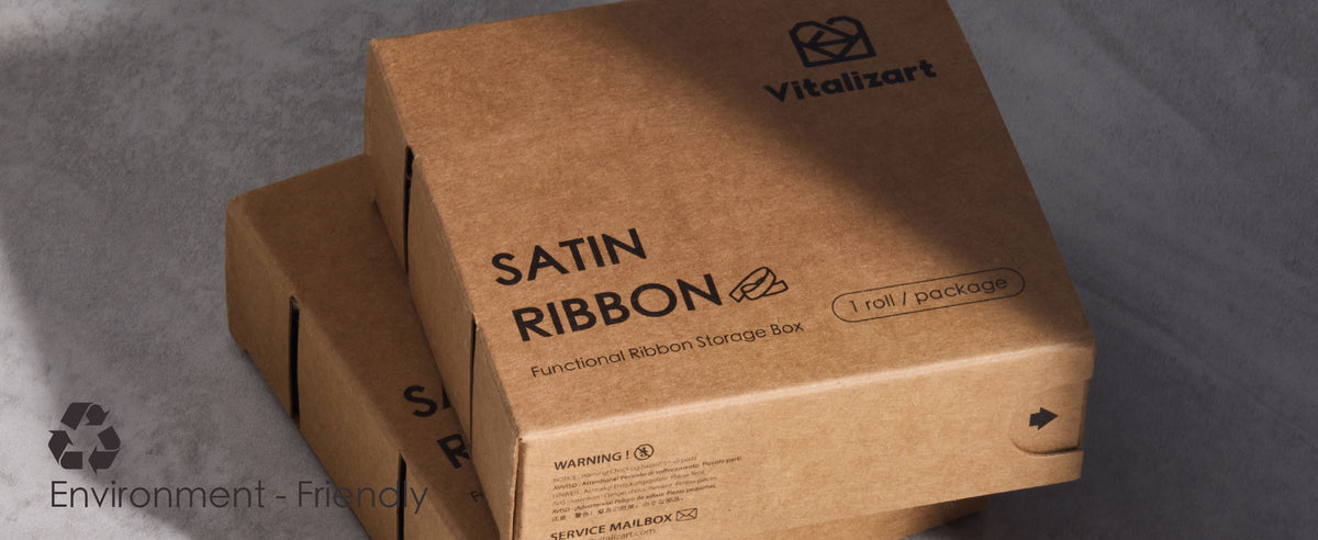 Two recyclable brown cardboard satin ribbon dispenser boxes stacked on softly lit gray fabric.