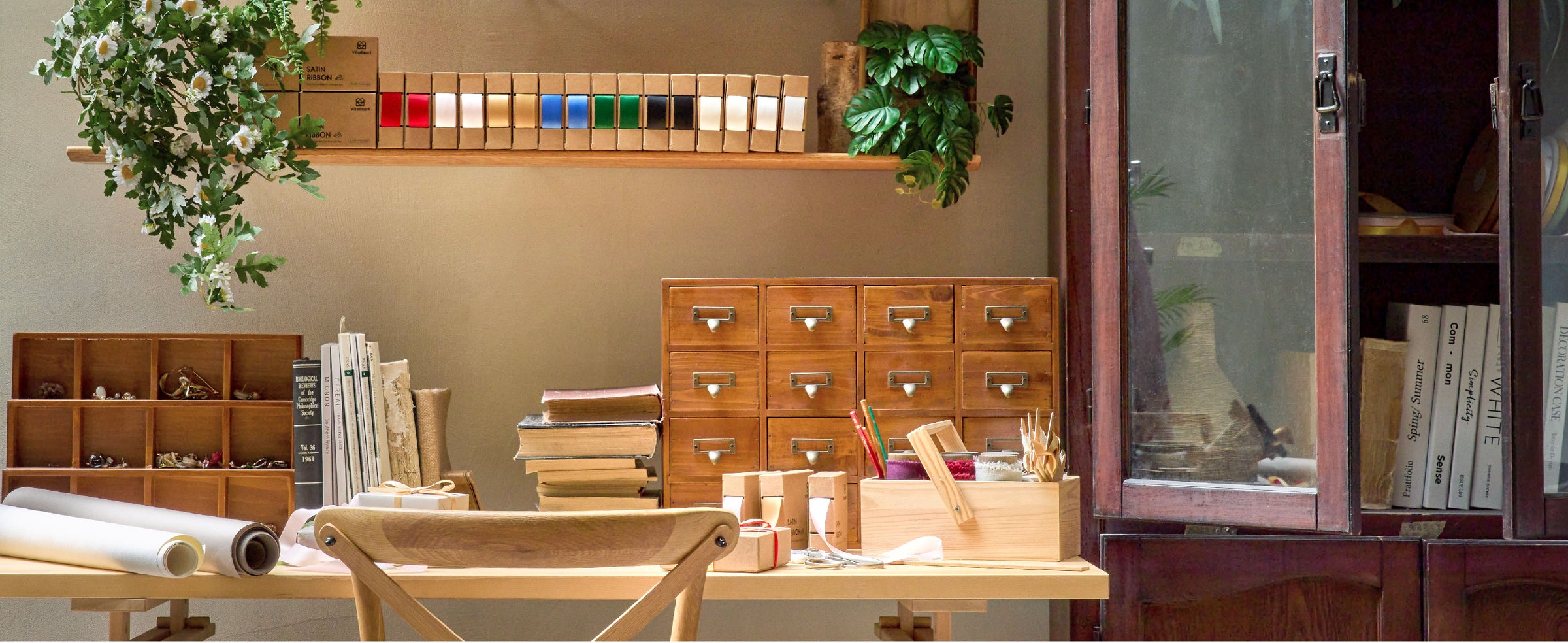 Sunlit craft studio with assorted ribbon dispensers, books, scissors, and supplies on a wooden worktable.