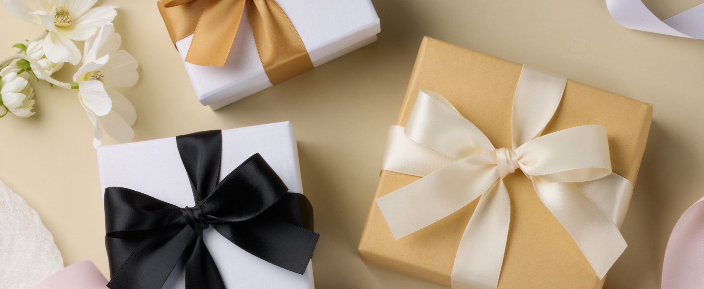 Gift boxes tied with gold, black, and ivory satin ribbon bows among flowers and loose ribbon