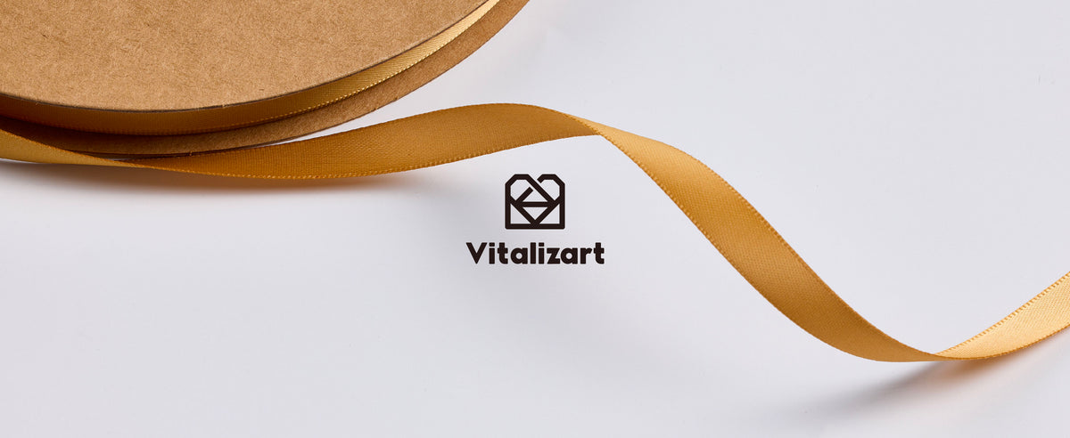 Narrow gold satin ribbon unwinding from a kraft spool around the centered Vitalizart logo