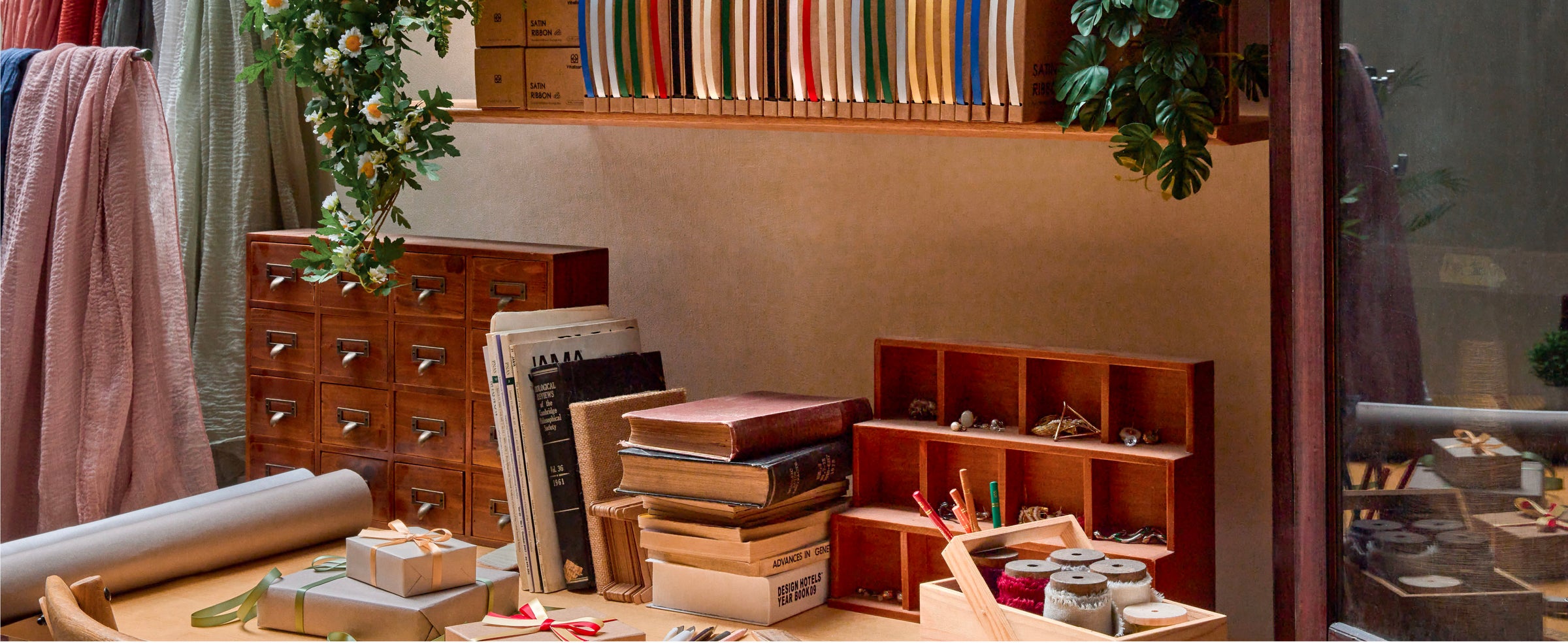 Assorted satin ribbon boxes displayed on a wooden craft-room shelf with books and supplies