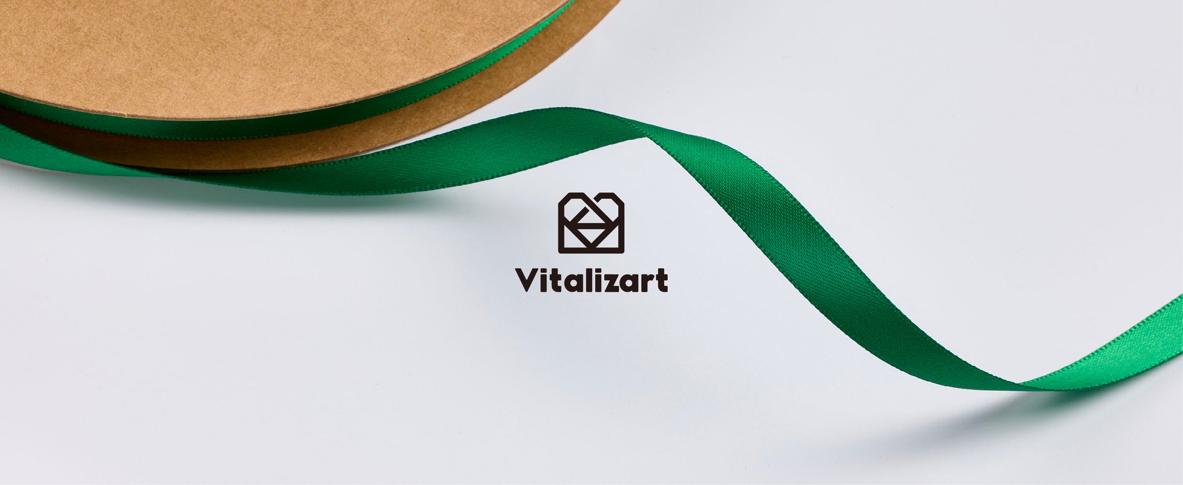 Glossy green satin ribbon unwinding from a kraft spool, with a close view of its woven texture