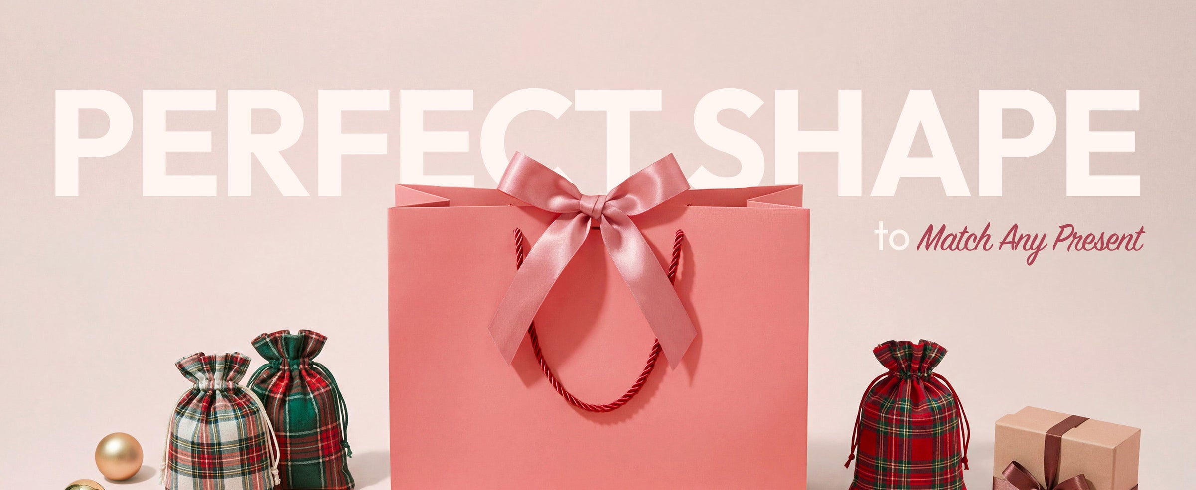 Coral-pink paper gift bag with satin bow among plaid pouches, wrapped boxes, and ornaments