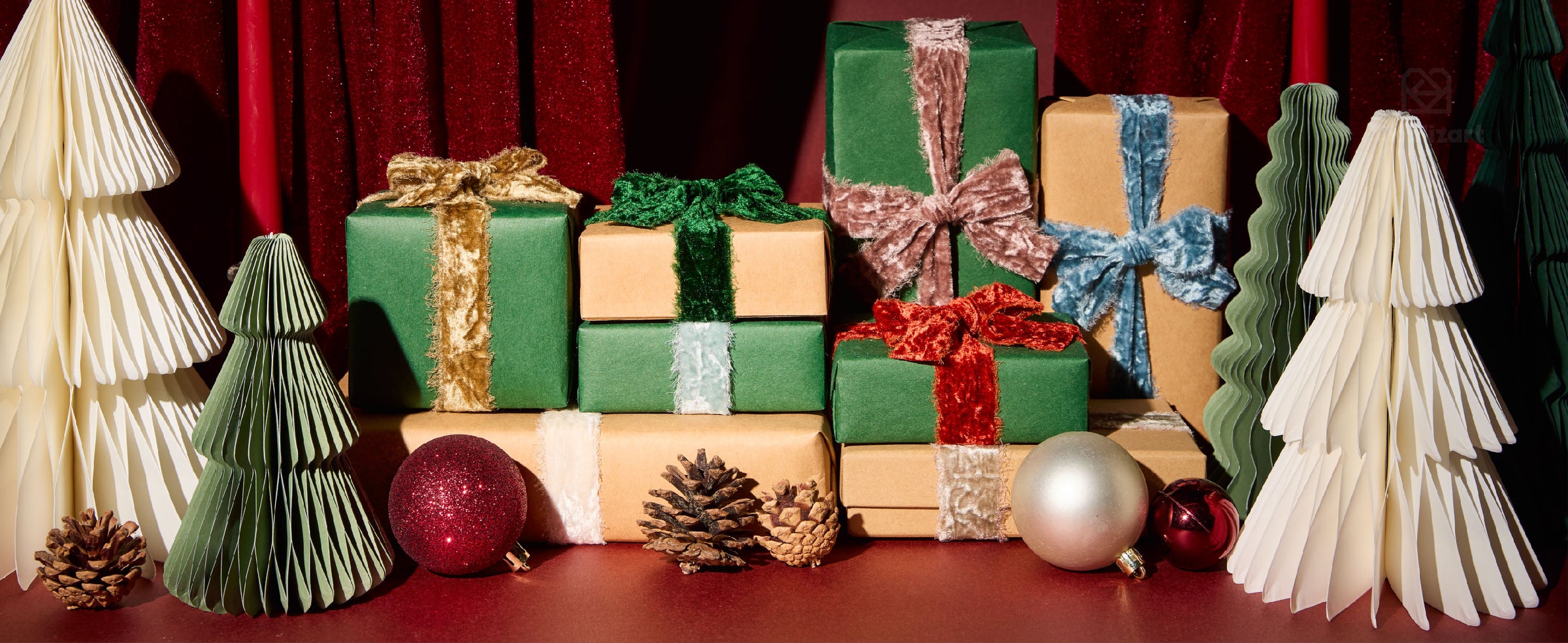 Christmas gifts tied with colorful frayed velvet ribbons, framed by candles, paper trees, and ornaments.