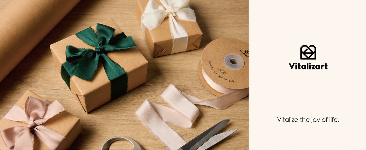 Frayed satin ribbon in ivory, blush, and green ties kraft gifts beside a ribbon spool and wrapping supplies.