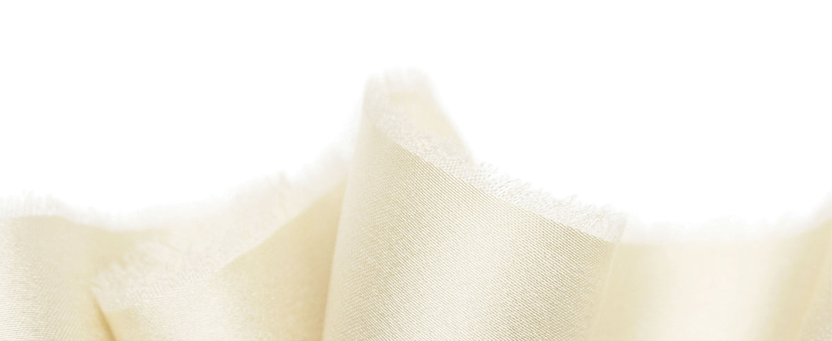 Ivory satin ribbon standing in soft waves, with a smooth woven surface and delicate frayed edge.