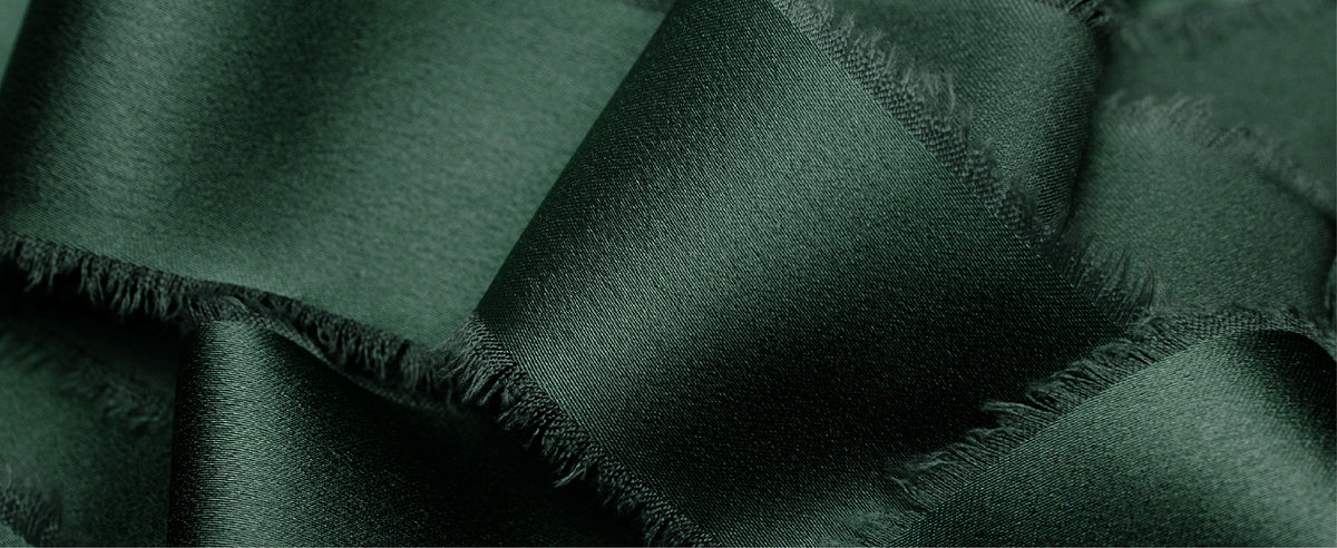 Close-up of dark green satin ribbon showing a lustrous woven texture and soft frayed edges
