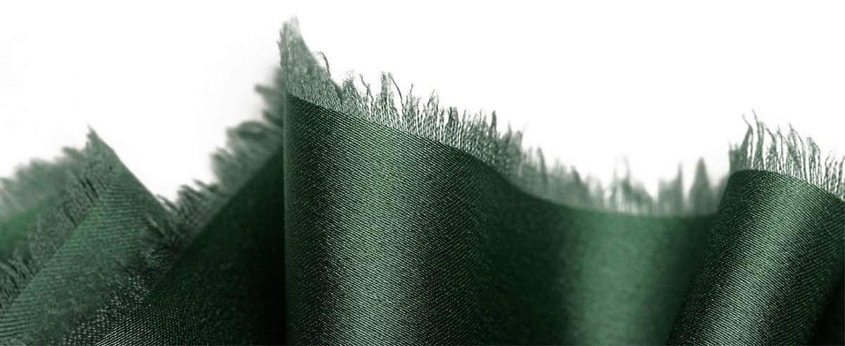 Dark green satin ribbon close-up highlighting its fine weave and irregular frayed edge