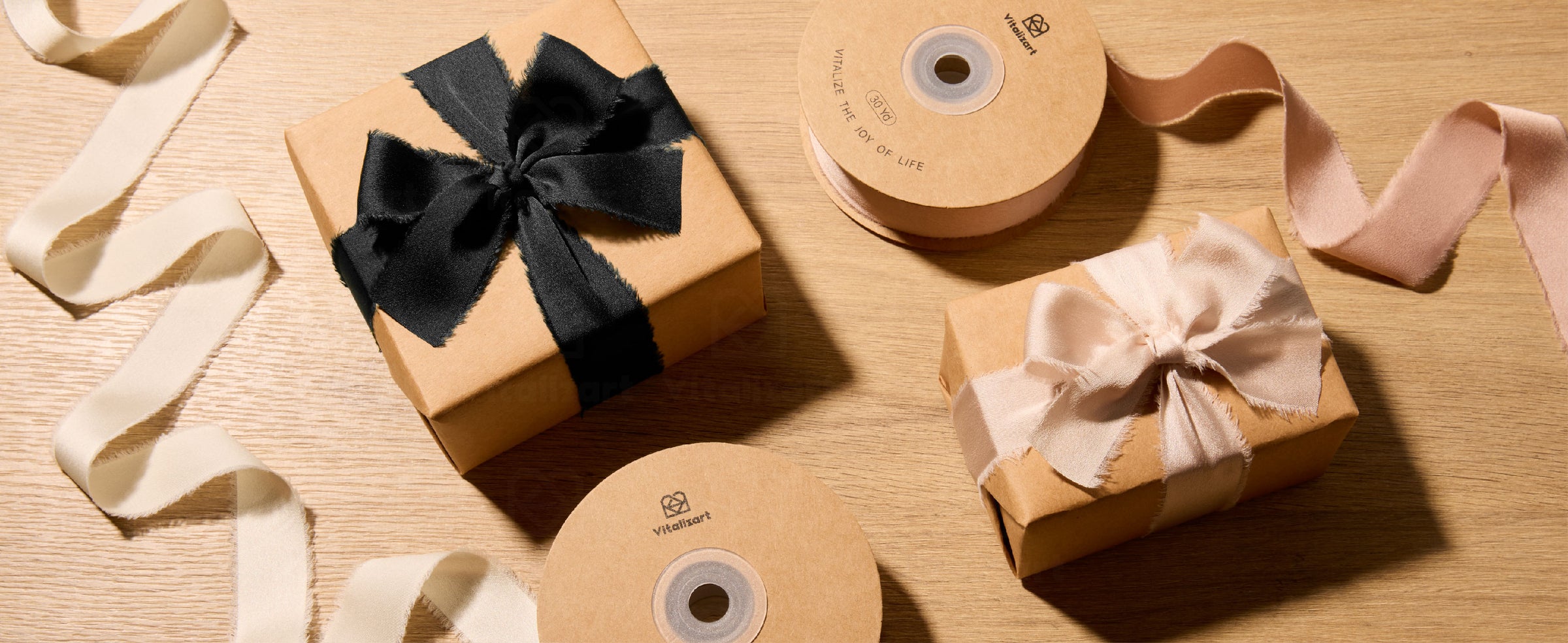Black and blush frayed satin ribbon bows on kraft gift boxes beside ribbon spools on a wood table.