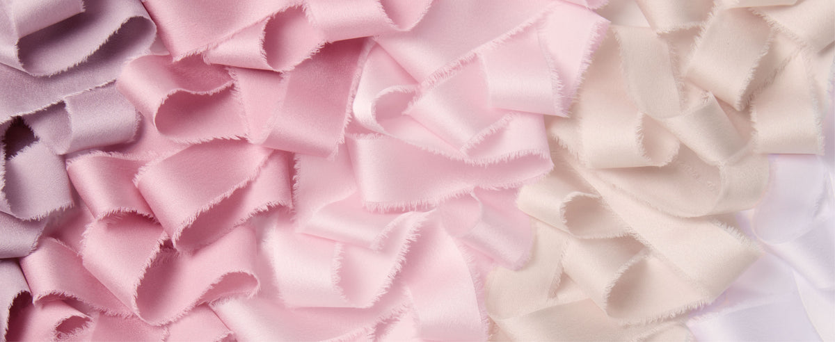 Close-up assortment of pink, nude, ivory, and lavender satin ribbon loops with soft frayed edges.