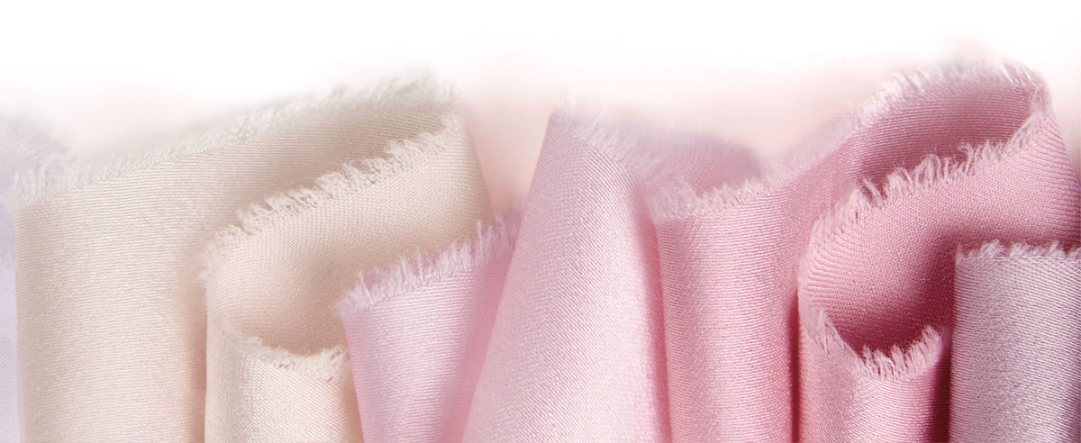 Pale pink, lavender, rose, and ivory satin ribbons with frayed edges arranged in soft upright folds.