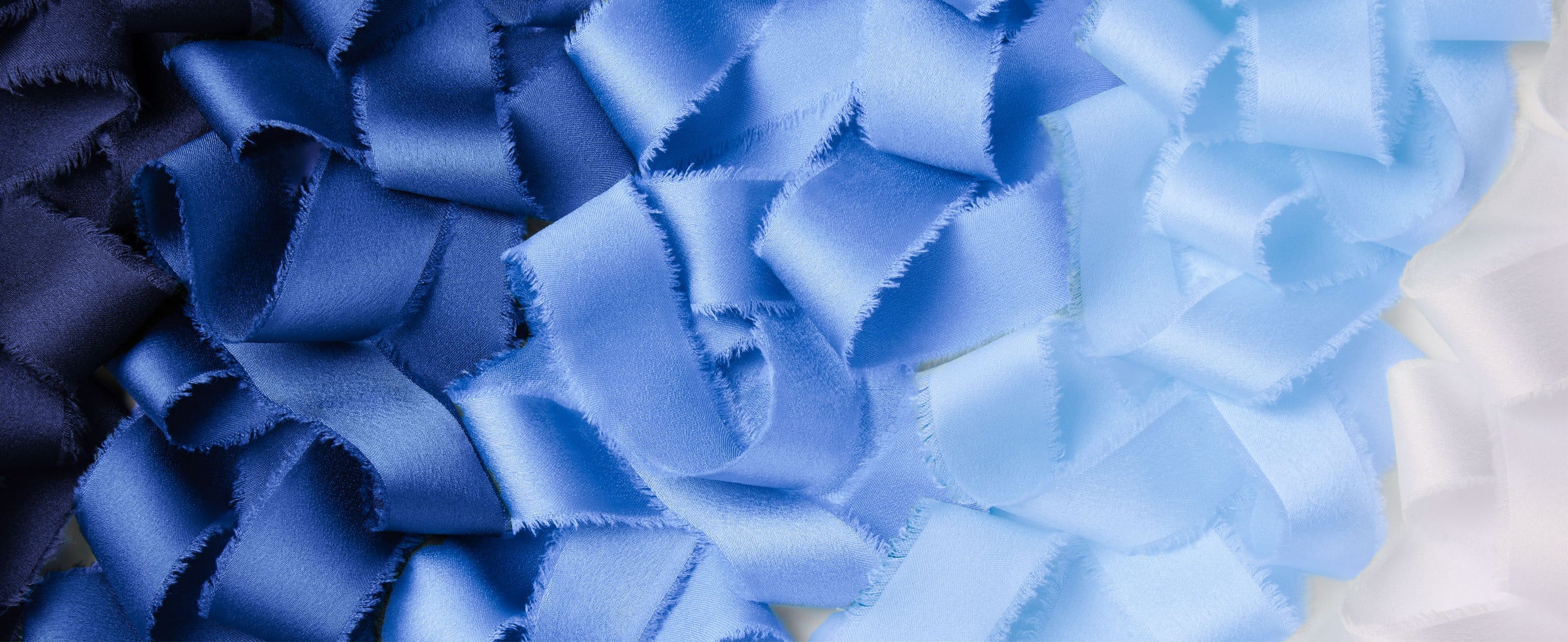 Loose frayed-edge satin ribbon in a gradient of navy, royal blue, pale blue, and white.