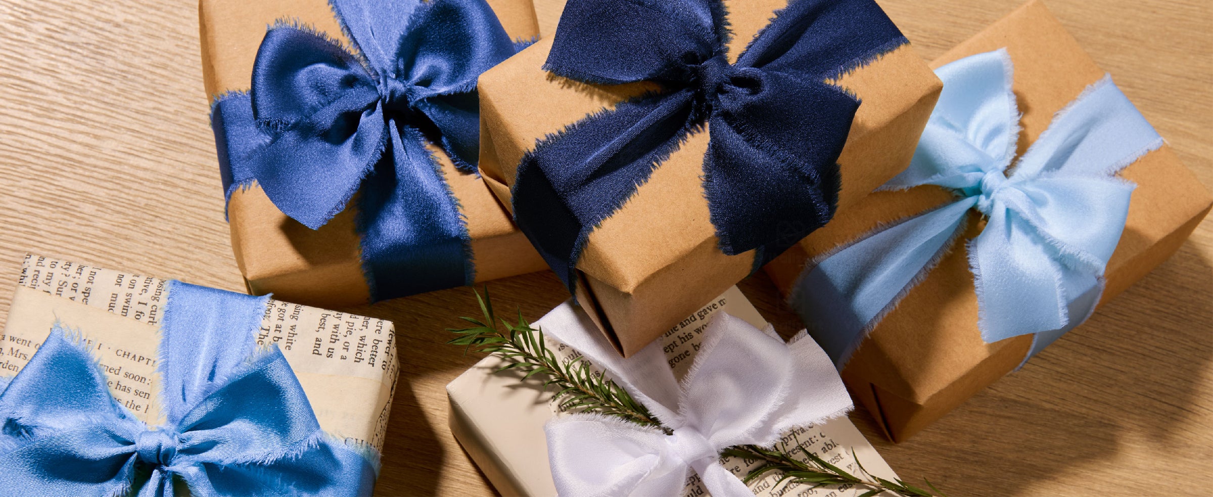 Kraft and white gifts tied with navy, blue, pale blue, and white frayed satin ribbon bows.