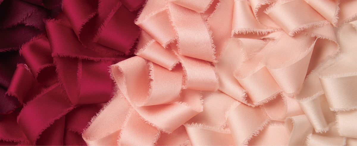 Burgundy, peach pink, and ivory satin ribbons layered in loose folds with soft frayed edges.