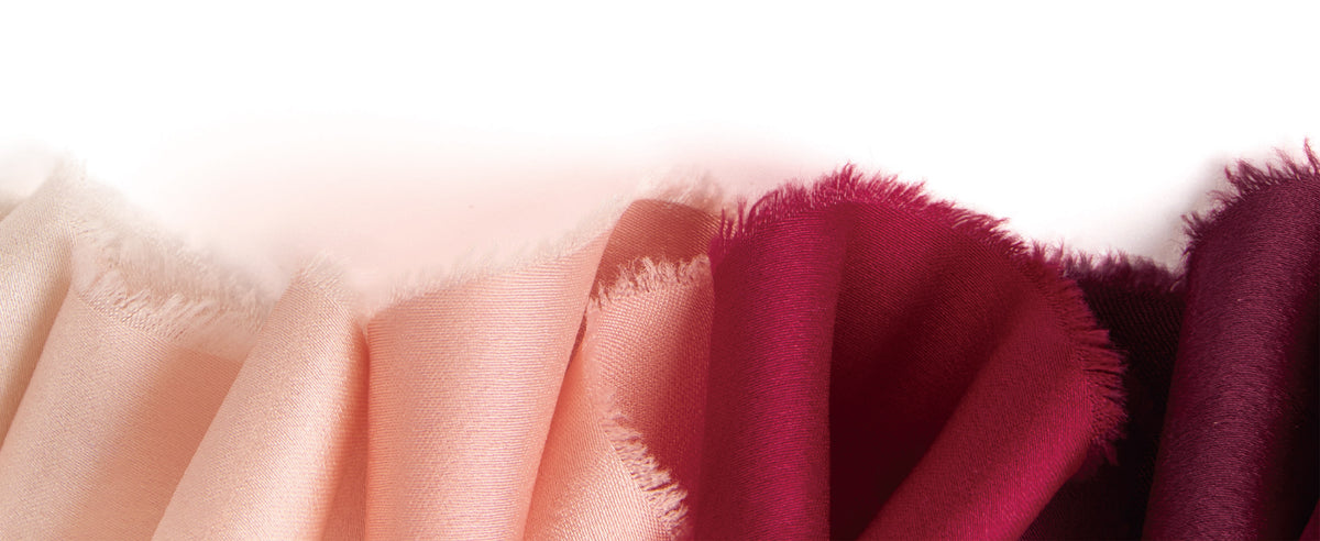 Close-up of pale pink, peach, and burgundy satin ribbon folds showing sheen and frayed edges.