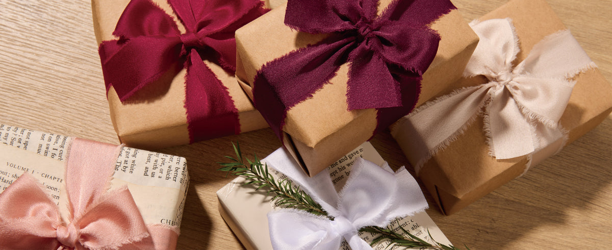 Kraft and white gift boxes tied with burgundy, peach, and white frayed satin ribbon bows.