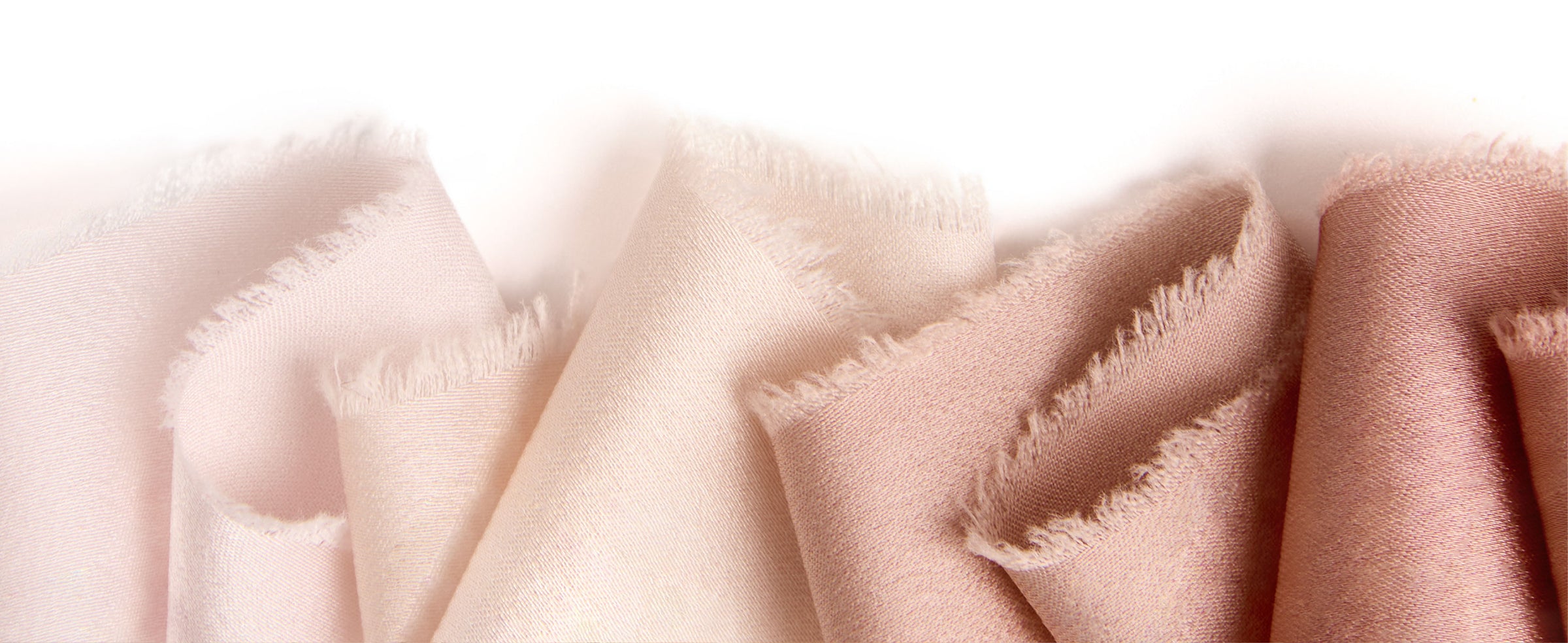 Close-up of white, ivory, and nude satin ribbon folds showing smooth sheen and frayed edges.