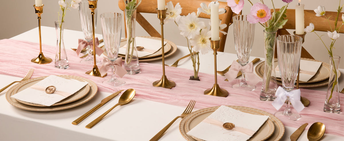 Nude, ivory, and white frayed satin ribbon accents on glasses and invitations at a floral table.