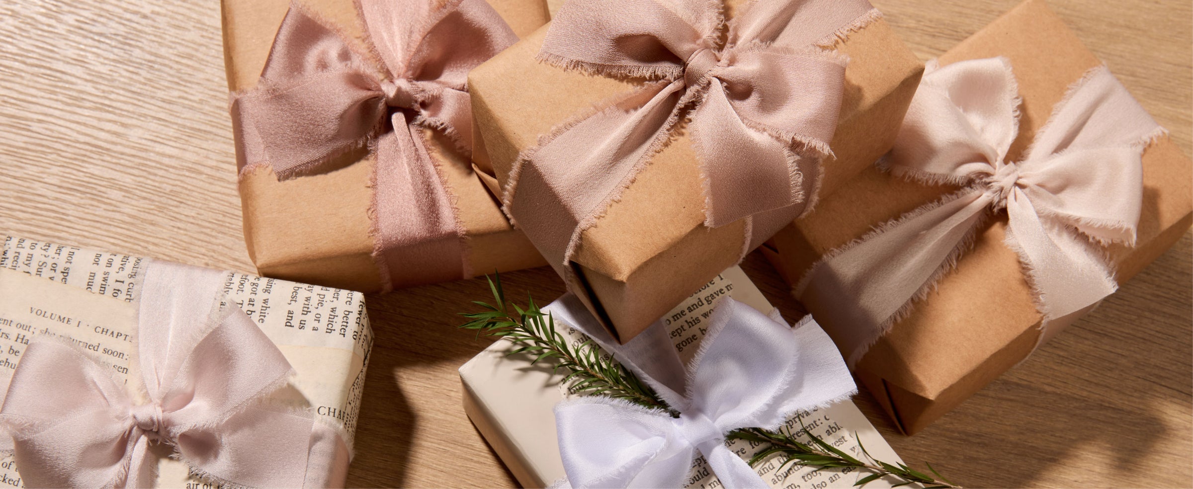 Kraft and white gift boxes tied with nude, ivory, and white frayed satin ribbon bows.