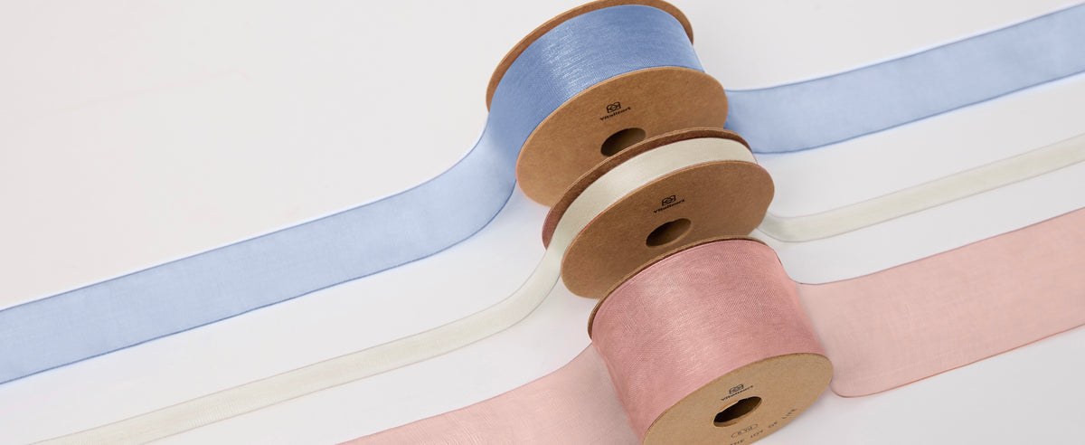Three spools of wide sheer organza ribbon in light blue, ivory and dusty pink on a white background