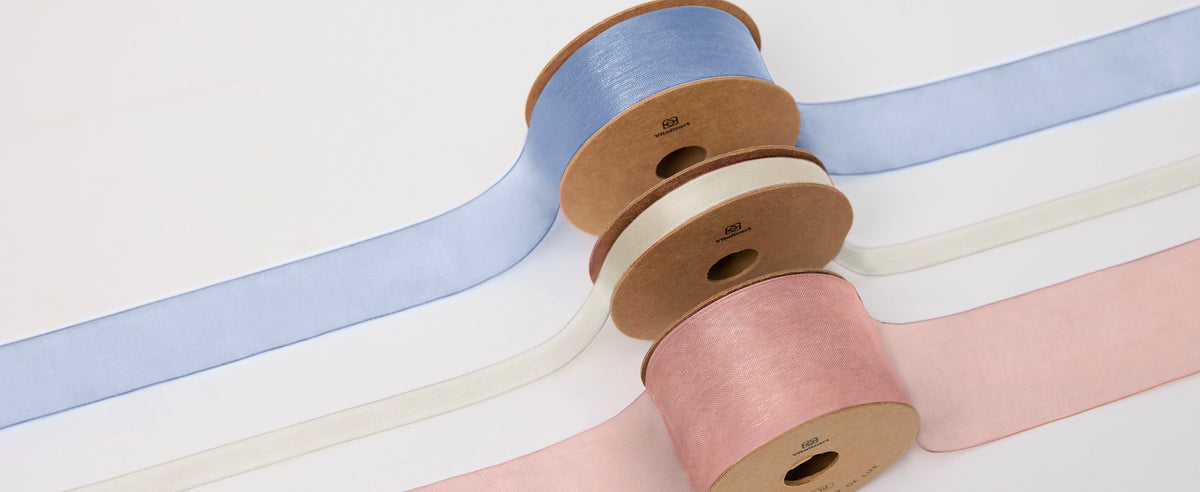 Three spools of wide sheer organza ribbon in light blue, ivory and dusty rose on a white background