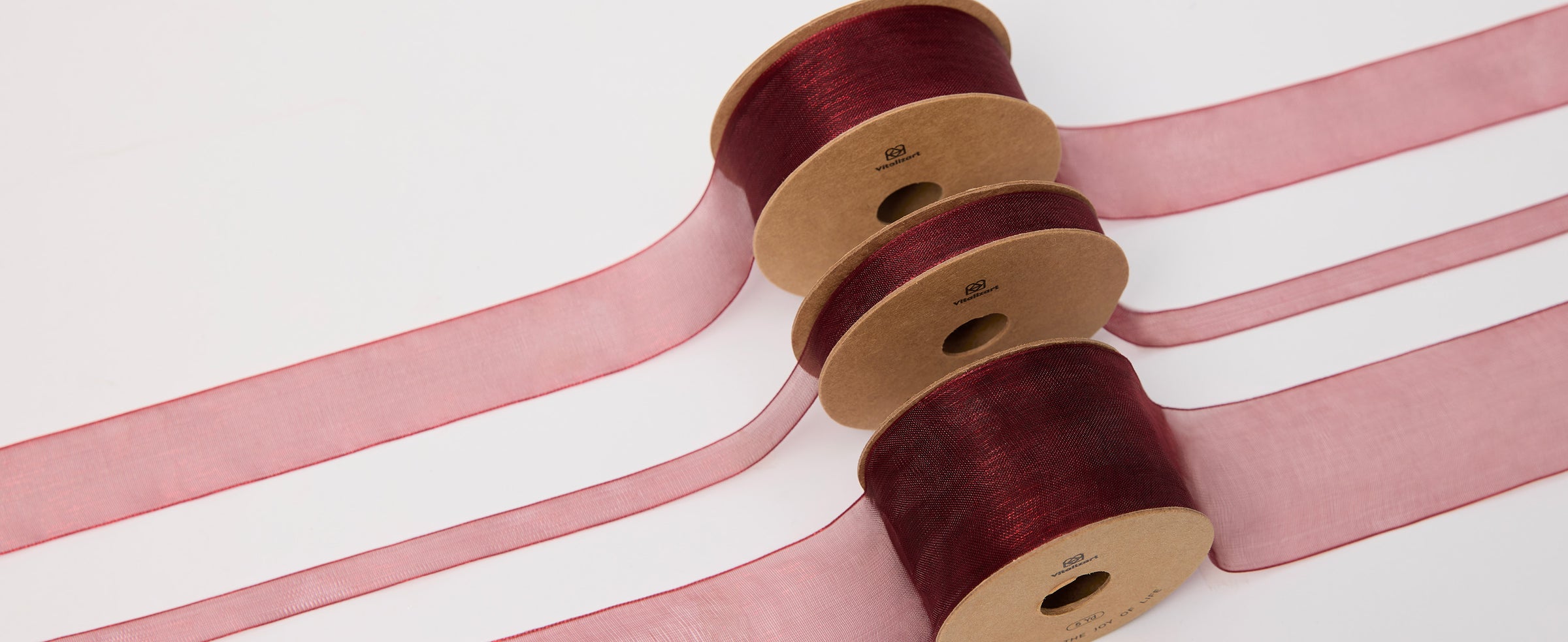 Three spools of sheer burgundy organza ribbon with loose lengths arranged on a white surface.