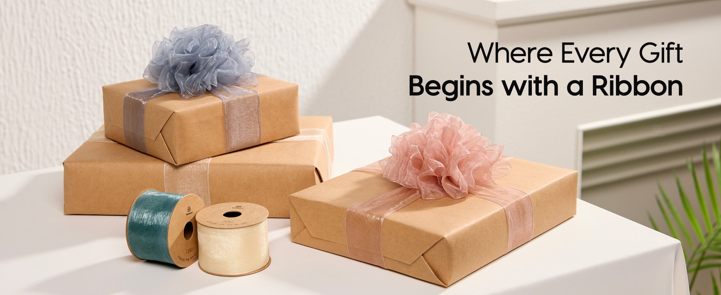 Kraft gifts tied with gray, ivory, and blush organza ribbon beside green and ivory spools