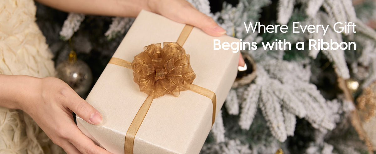 Hands wrapping a gift box with the mixed cream, rose gold, and green organza ribbon set beside festive greenery