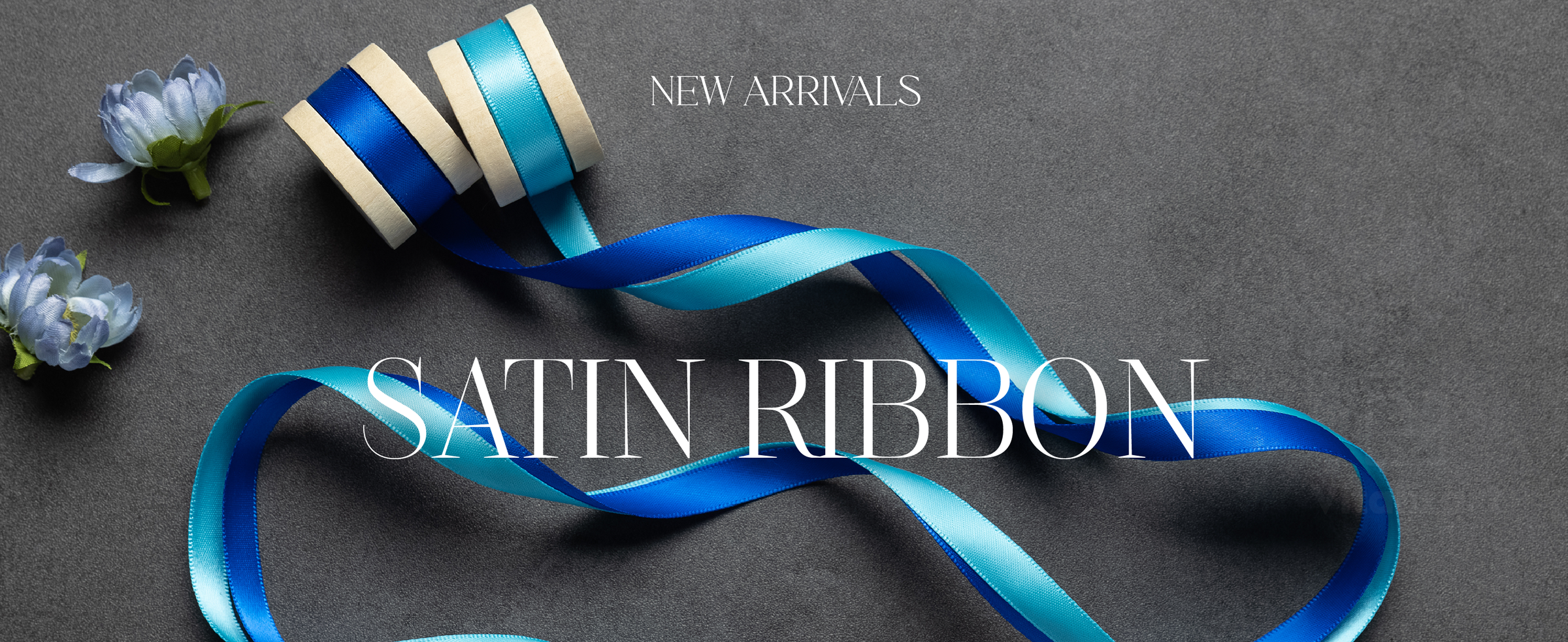 Royal blue and turquoise satin ribbons unwind from pale wooden spools among blue flowers.