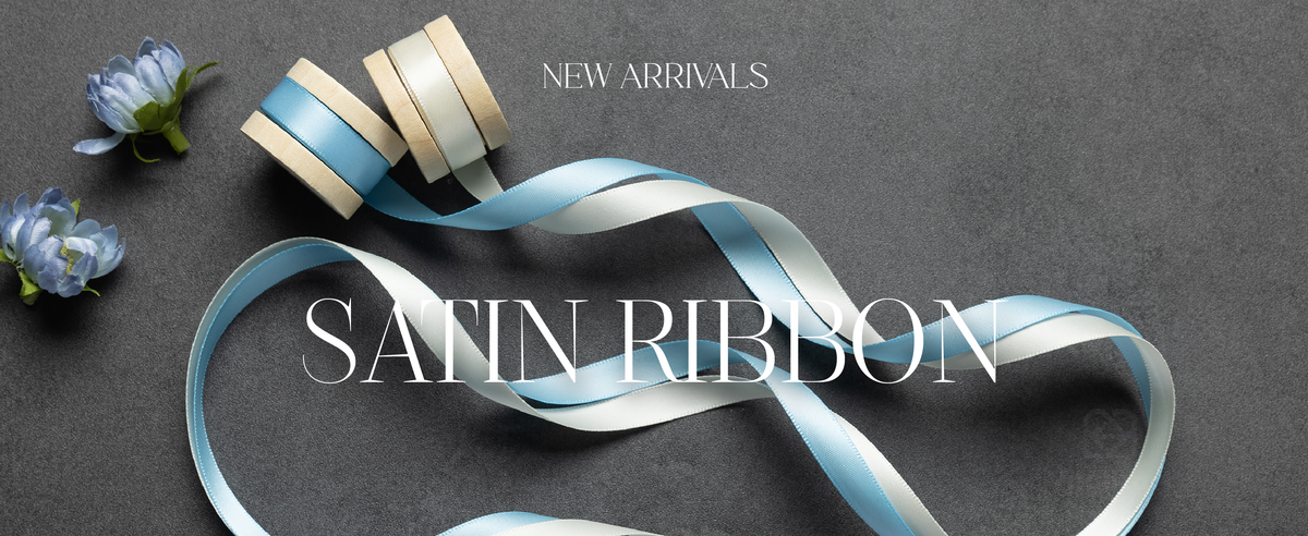Light blue and white satin ribbons unwind from wooden spools among pale blue flowers.