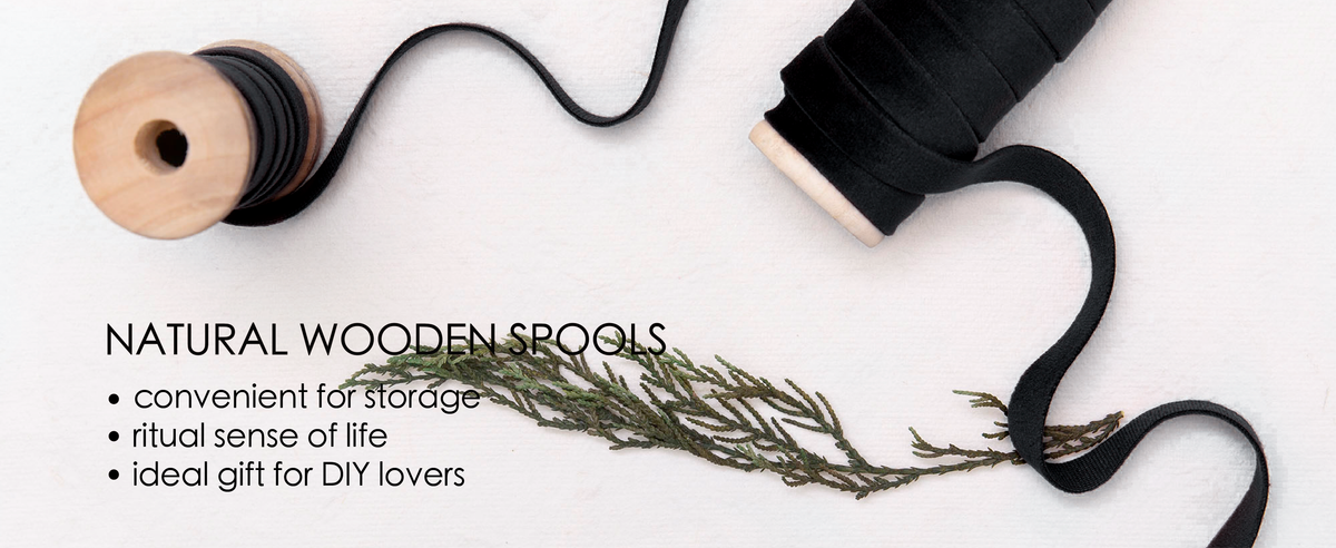 Black velvet ribbon unwinds between two natural wooden spools on a white surface