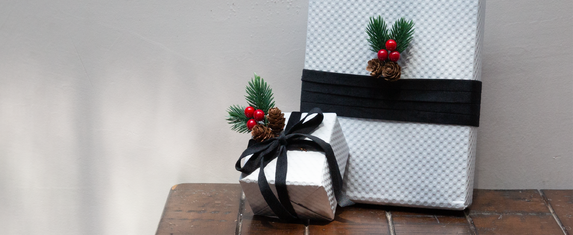 White holiday gift boxes wrapped with black velvet ribbon, pine sprigs, berries, and pinecones