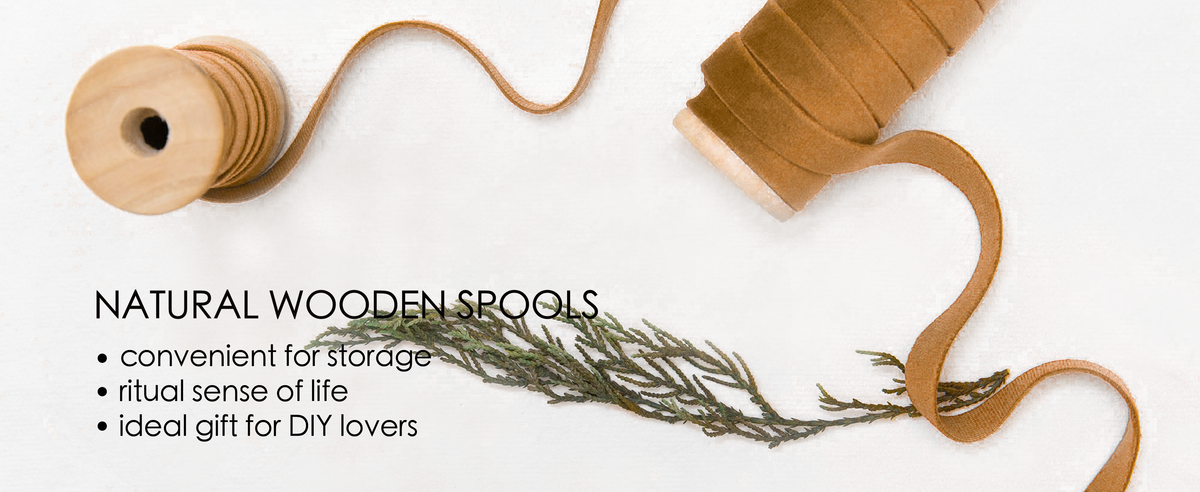 Khaki velvet ribbon wound on natural wooden spools, with a loose strand and dried greenery.