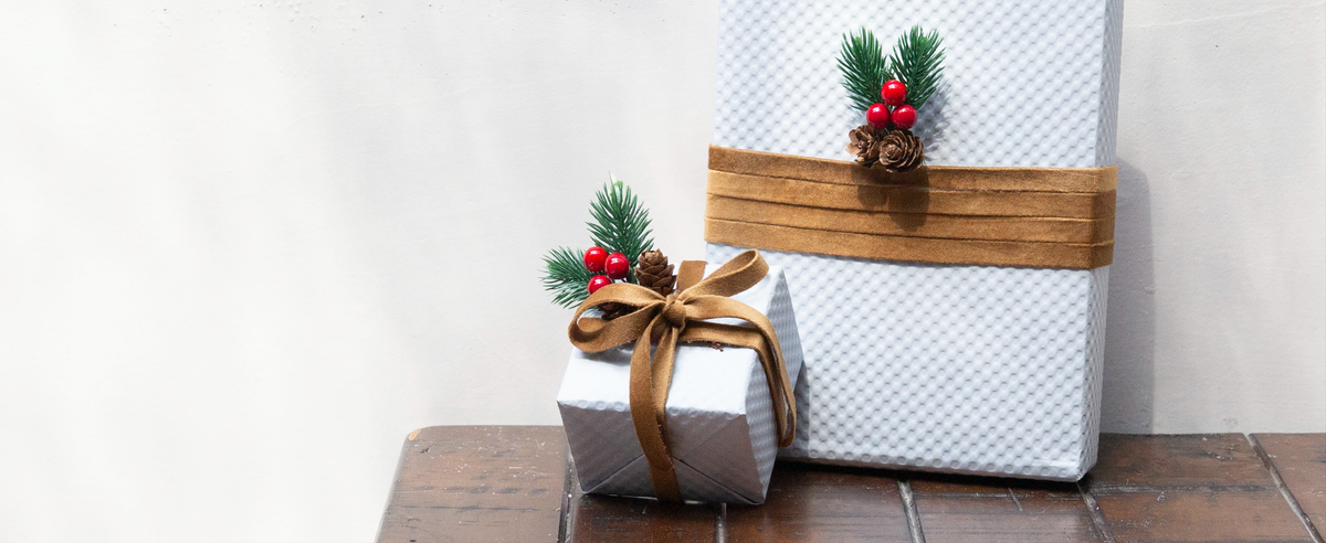 White holiday gifts wrapped with khaki velvet ribbon, pinecones, evergreen sprigs, and red berries.