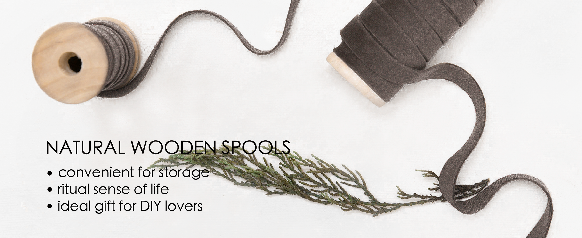 Gray velvet ribbon wound on natural wooden spools with a loose strand and botanical sprig.
