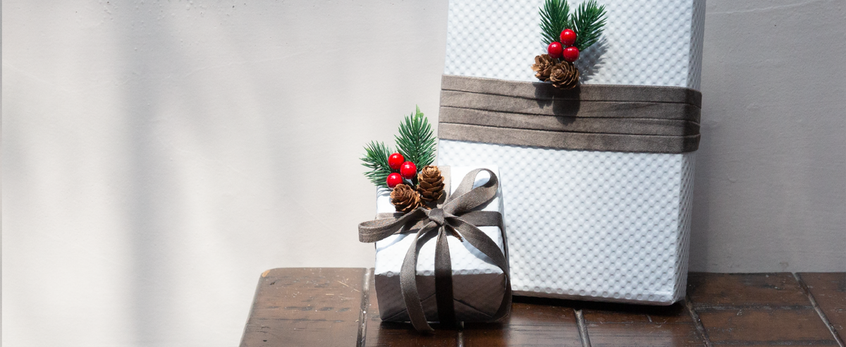 White gift boxes wrapped with gray velvet ribbon, pine sprigs, red berries, and pinecones.