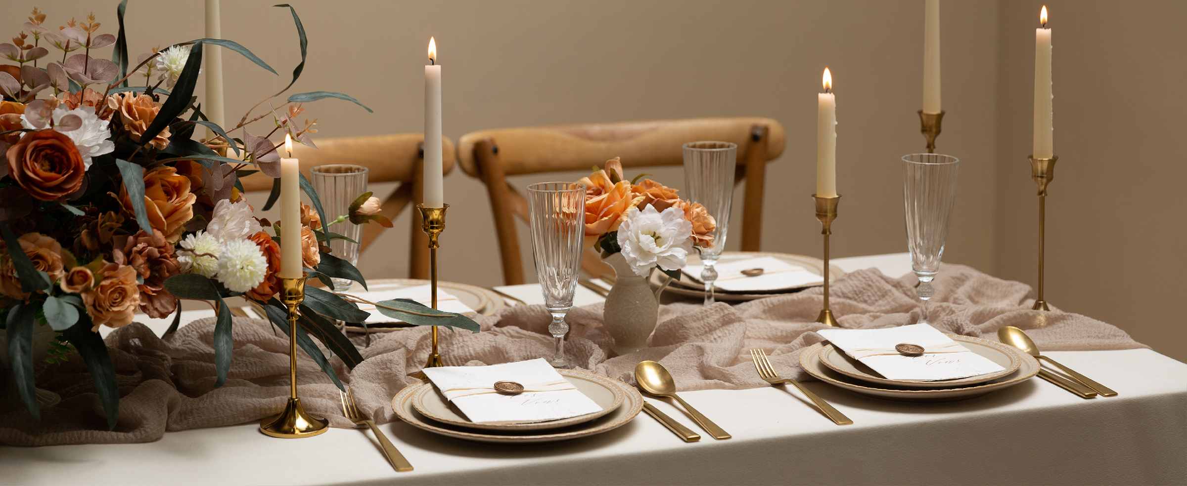 Ivory ribbon accents formal place settings with gold flatware, orange flowers, and lit taper candles.