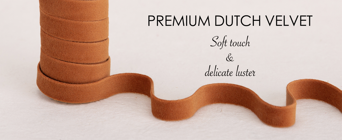 Terracotta, gray and tan velvet ribbons wound on natural wooden spools over cream fabric.