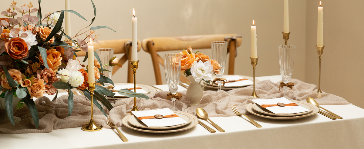 Orange velvet ribbon wraps invitations while brown bows accent glasses on a candlelit floral table.