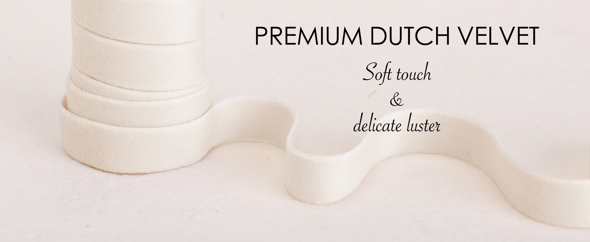 Khaki, ivory, and gray-nude velvet ribbons wound on natural wooden spools over cream fabric.