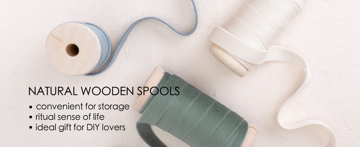 Dusty blue, ivory, and dusty green velvet ribbons on natural wooden spools over cream fabric.