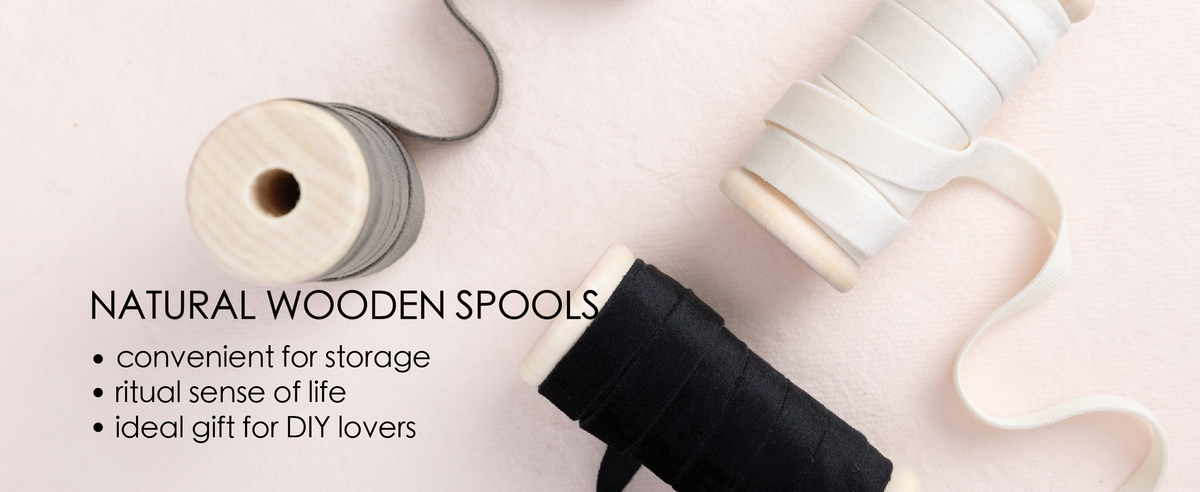 Black, gray, and white velvet ribbon set unwound from natural wooden spools in a clean product detail scene